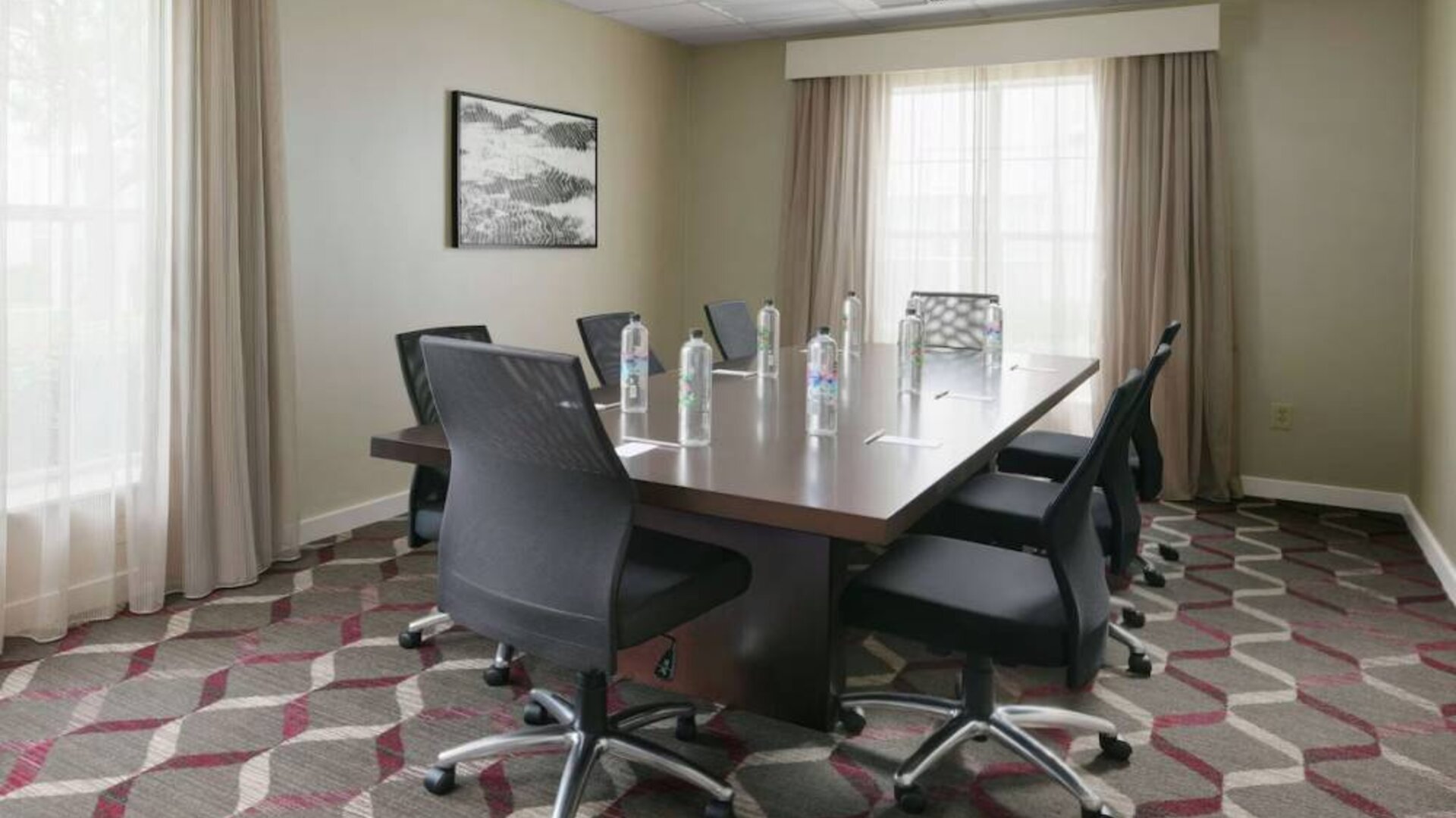 Meeting room in Sonesta ES Suites Fort Worth Fossil Creek, furnished with long wooden table and eight swivel chairs.