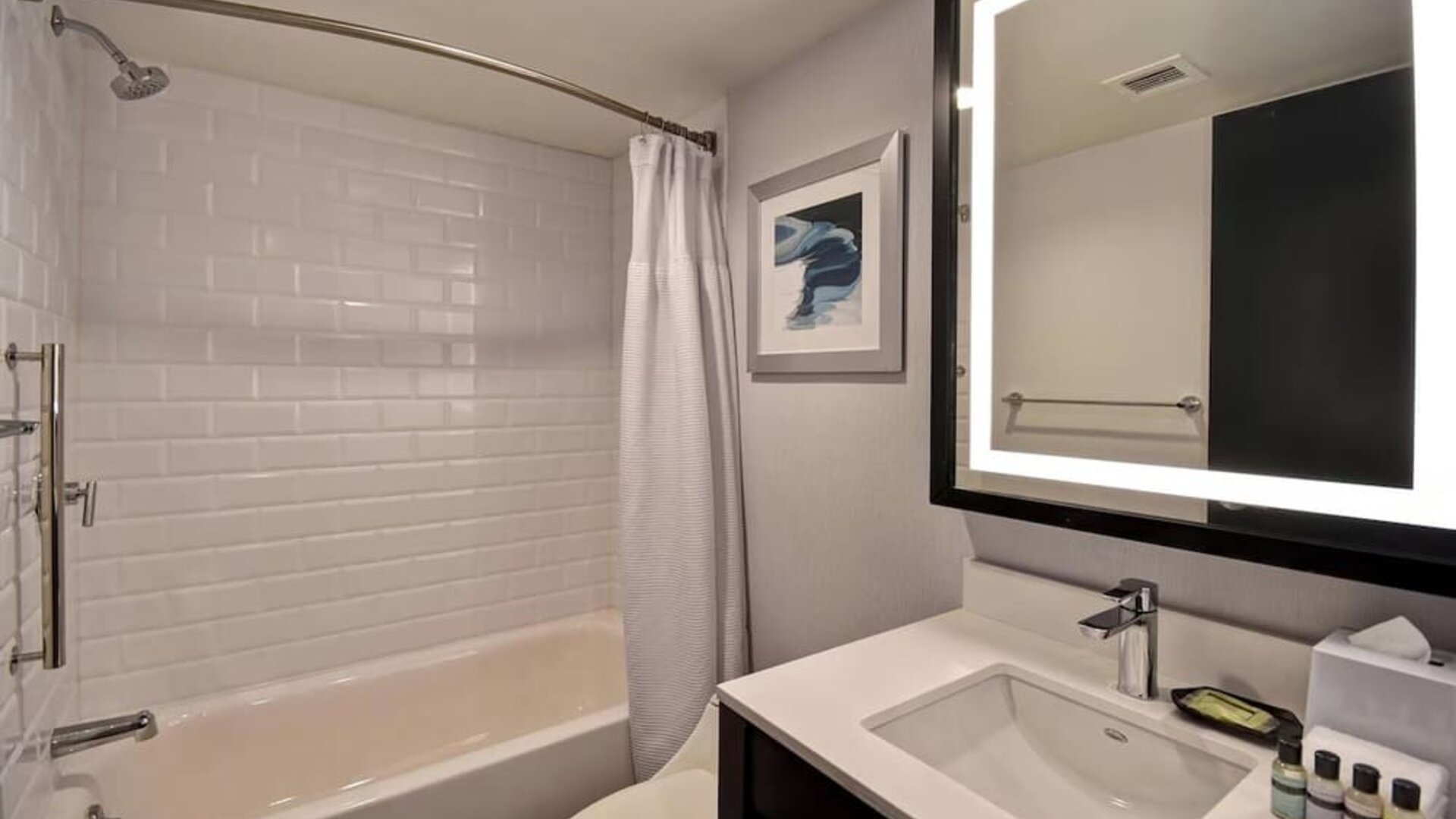 Modern guest bathroom featuring a sleek vanity, illuminated mirror, premium bath amenities, and a tub-shower combination at Four Points by Sheraton Boston-Newton.