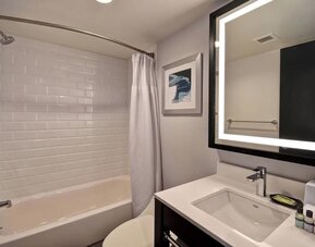 Modern guest bathroom featuring a sleek vanity, illuminated mirror, premium bath amenities, and a tub-shower combination at Four Points by Sheraton Boston-Newton.