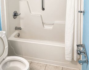 Accessible guest bathroom featuring a tub-shower combination, safety grab bars, and mobility-friendly design elements for enhanced comfort at Blue Way Inn & Suites Wichita East.