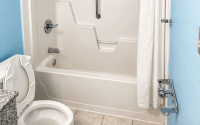 Accessible guest bathroom featuring a tub-shower combination, safety grab bars, and mobility-friendly design elements for enhanced comfort at Blue Way Inn & Suites Wichita East.