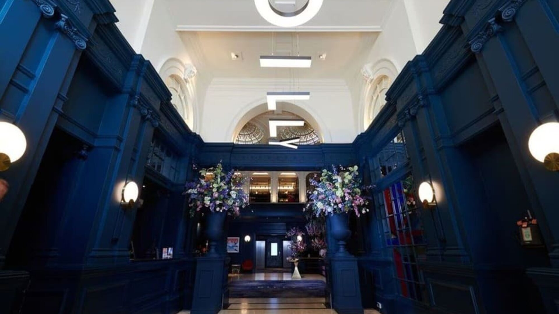 Hotel entrance with bold navy walls and modern hanging letter lights at The Dilly.  