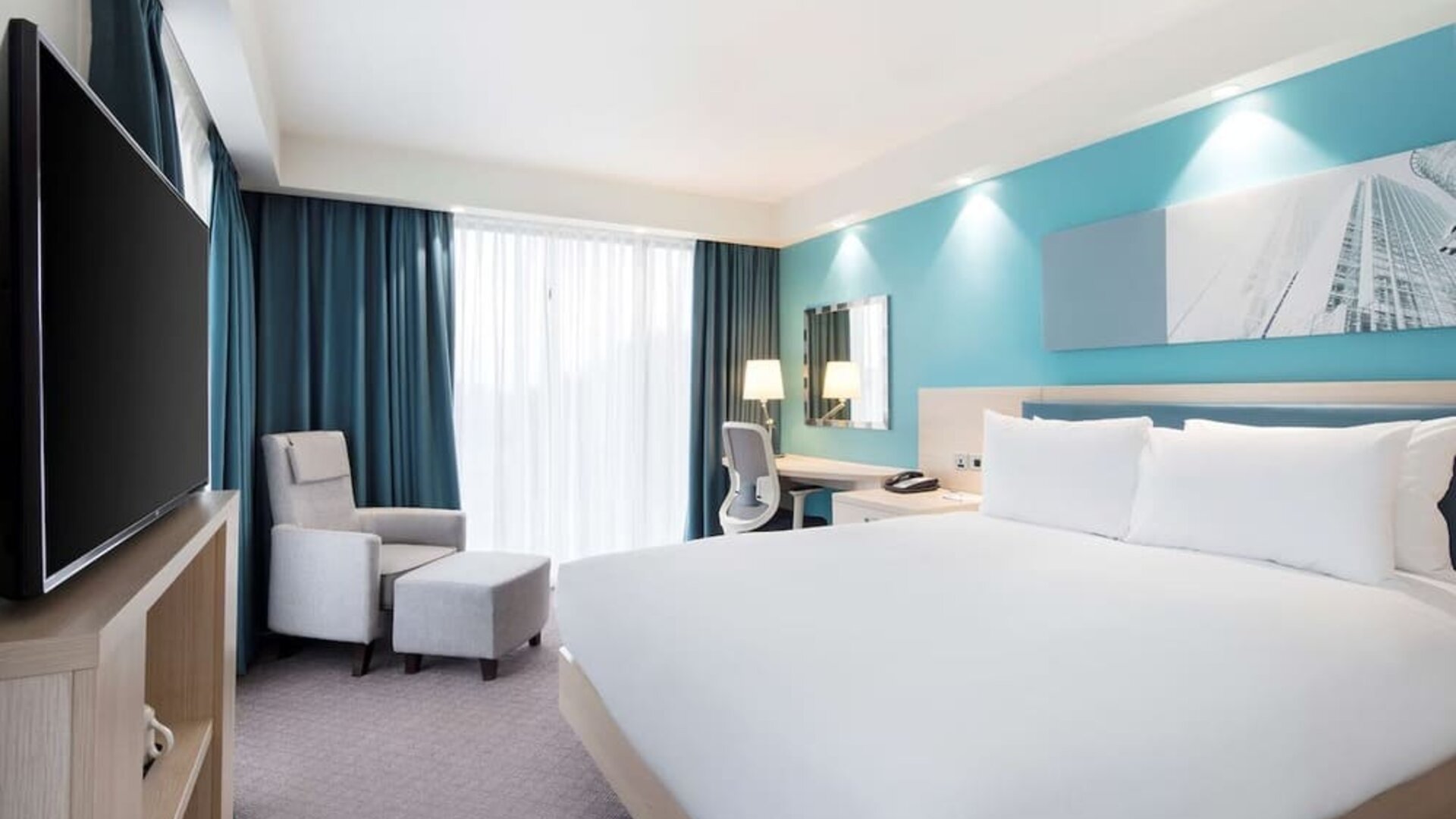 King bedroom with work desk, TV and sofa at the Hampton by Hilton London Docklands.