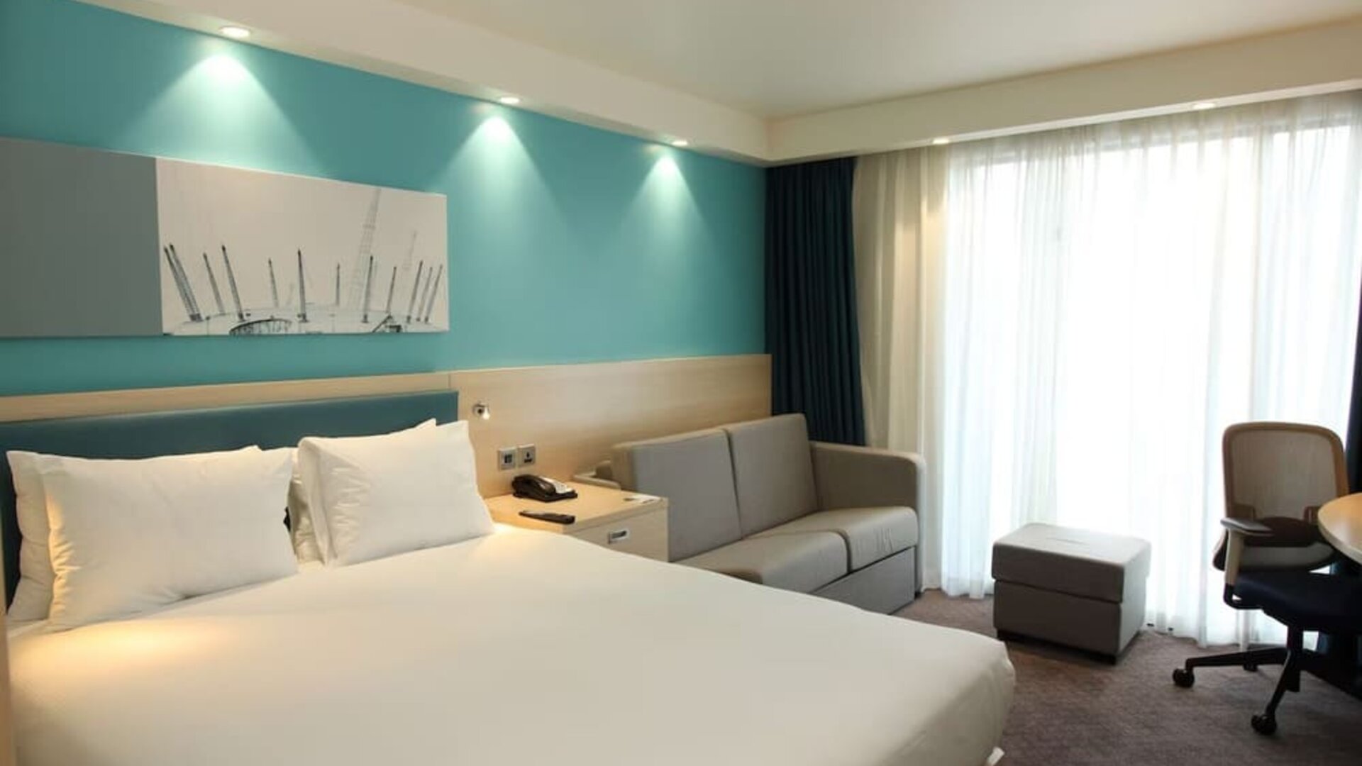 Day use room with king bed, work desk and sofa at the Hampton by Hilton London Docklands.