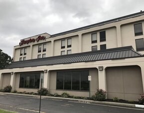 Exterior entrance of Hampton Inn Ridgefield Park featuring a covered porte-cochère, landscaped grounds, and convenient guest parking.
