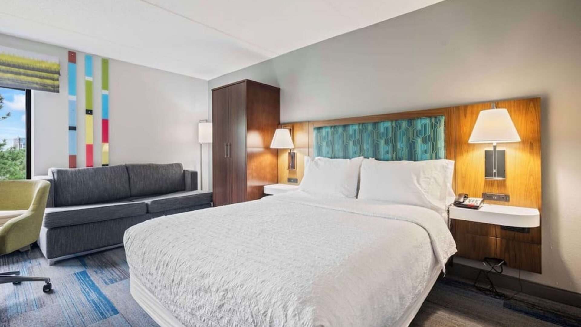 Bright guest room featuring a comfortable king bed, sofa seating, large windows, and modern amenities for a relaxing stay at Hampton Inn Ridgefield Park.