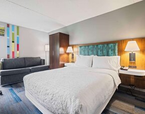 Bright guest room featuring a comfortable king bed, sofa seating, large windows, and modern amenities for a relaxing stay at Hampton Inn Ridgefield Park.