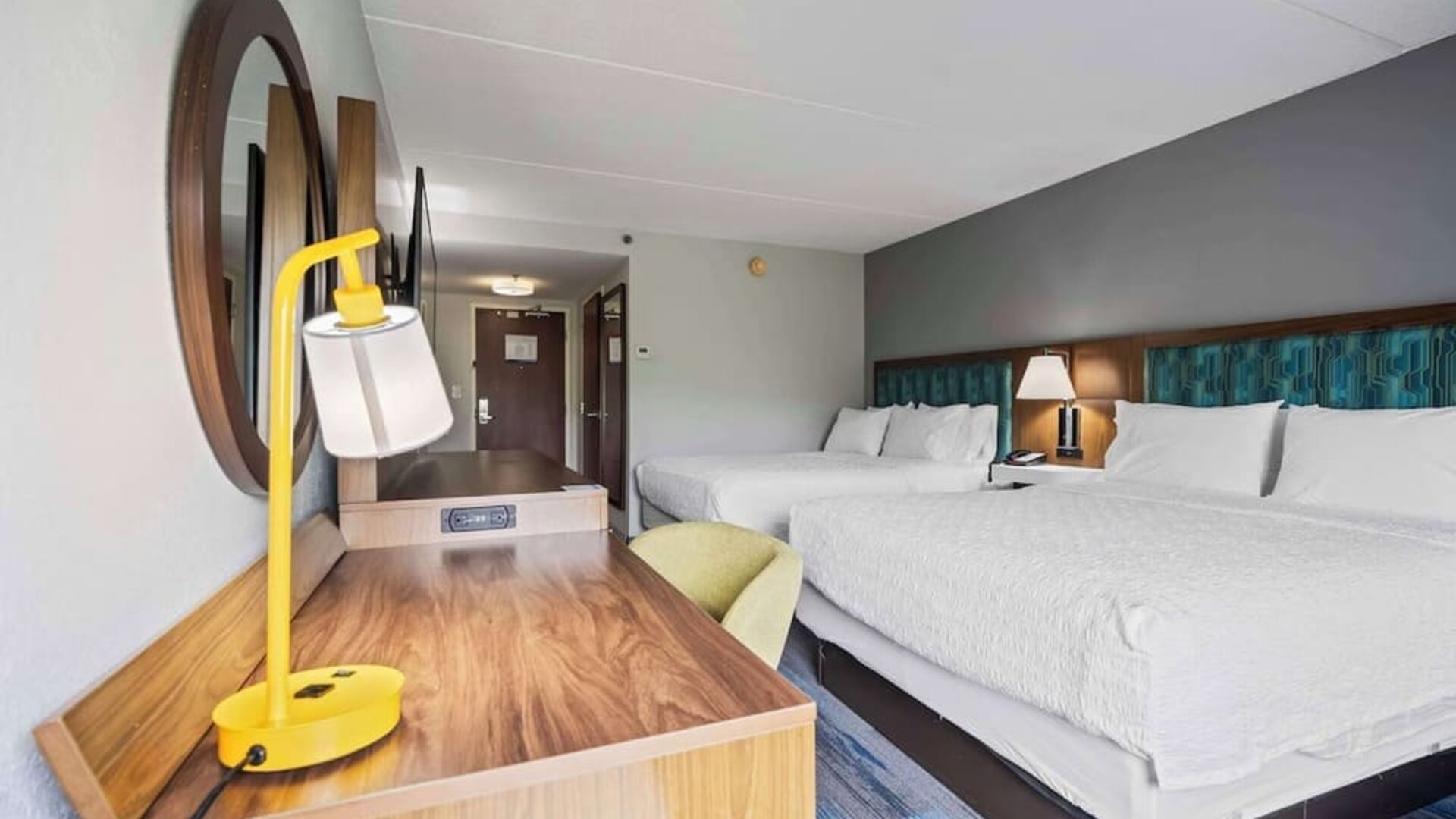 Double Queen guest room featuring two plush Hampton beds, a spacious work desk, comfortable seating, modern furnishings, and thoughtful amenities for a relaxing stay at Hampton Inn Ridgefield Park.