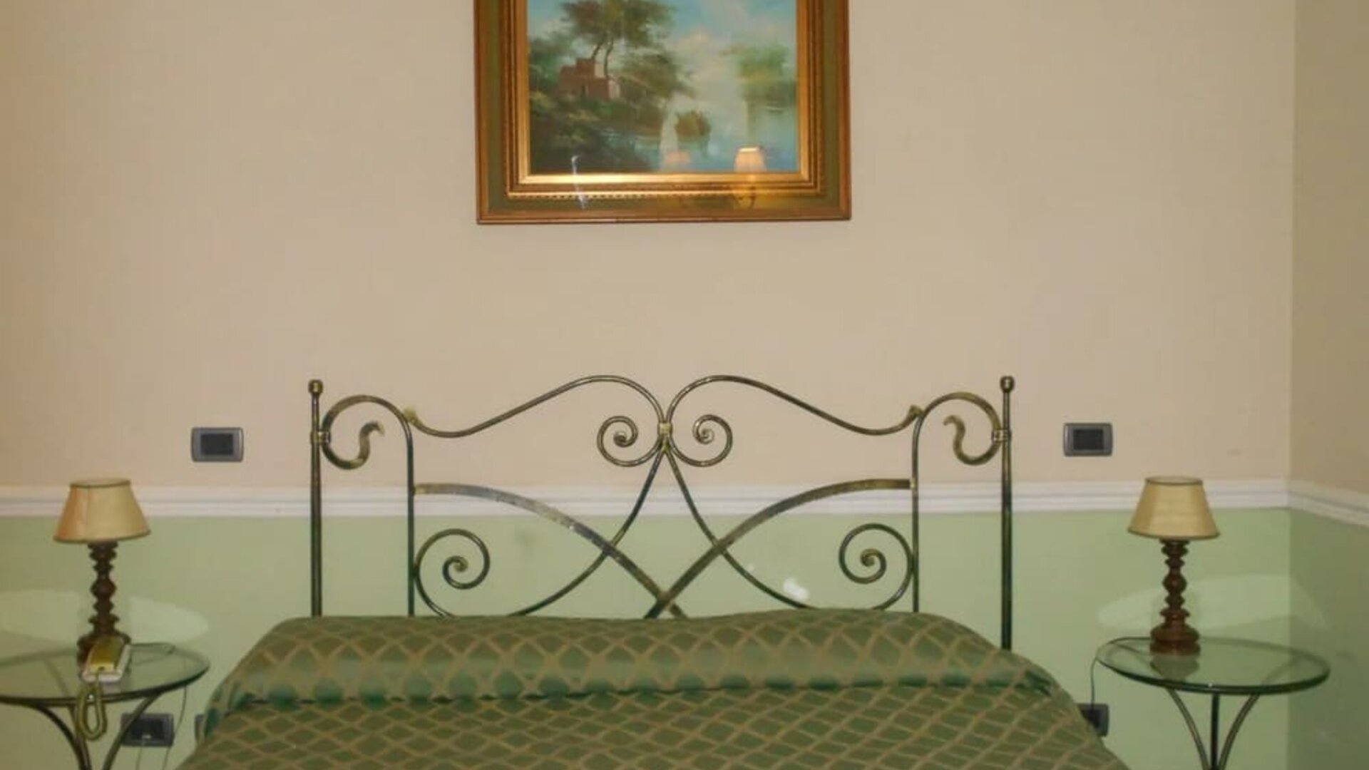 Comfortable guest room with a wrought-iron bed, soft green accents, and classic Italian styling.