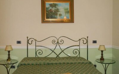 Comfortable guest room with a wrought-iron bed, soft green accents, and classic Italian styling.