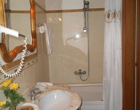 Bright bathroom with a marble vanity, bathtub with shower, hairdryer, and complimentary toiletries.