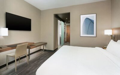 Modern guest room featuring a plush king bed, dedicated workspace, wall-mounted TV, contemporary furnishings, and a bright, minimalist design.