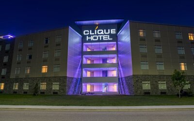 Hotel exterior at night with illuminated Clique Hotel signage and purple accent lighting on the central entrance. Hotel Clique Calgary Airport.