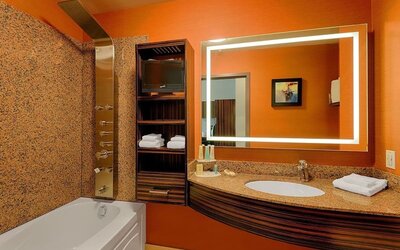 Bathroom with soaking tub, rainfall shower panel, illuminated mirror, granite vanity, and open shelving. Hotel Clique Calgary Airport.