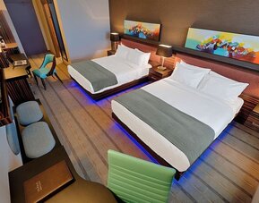 Guest room with two queen beds, workspace, seating area, and contemporary artwork above each headboard. Hotel Clique Calgary Airport.