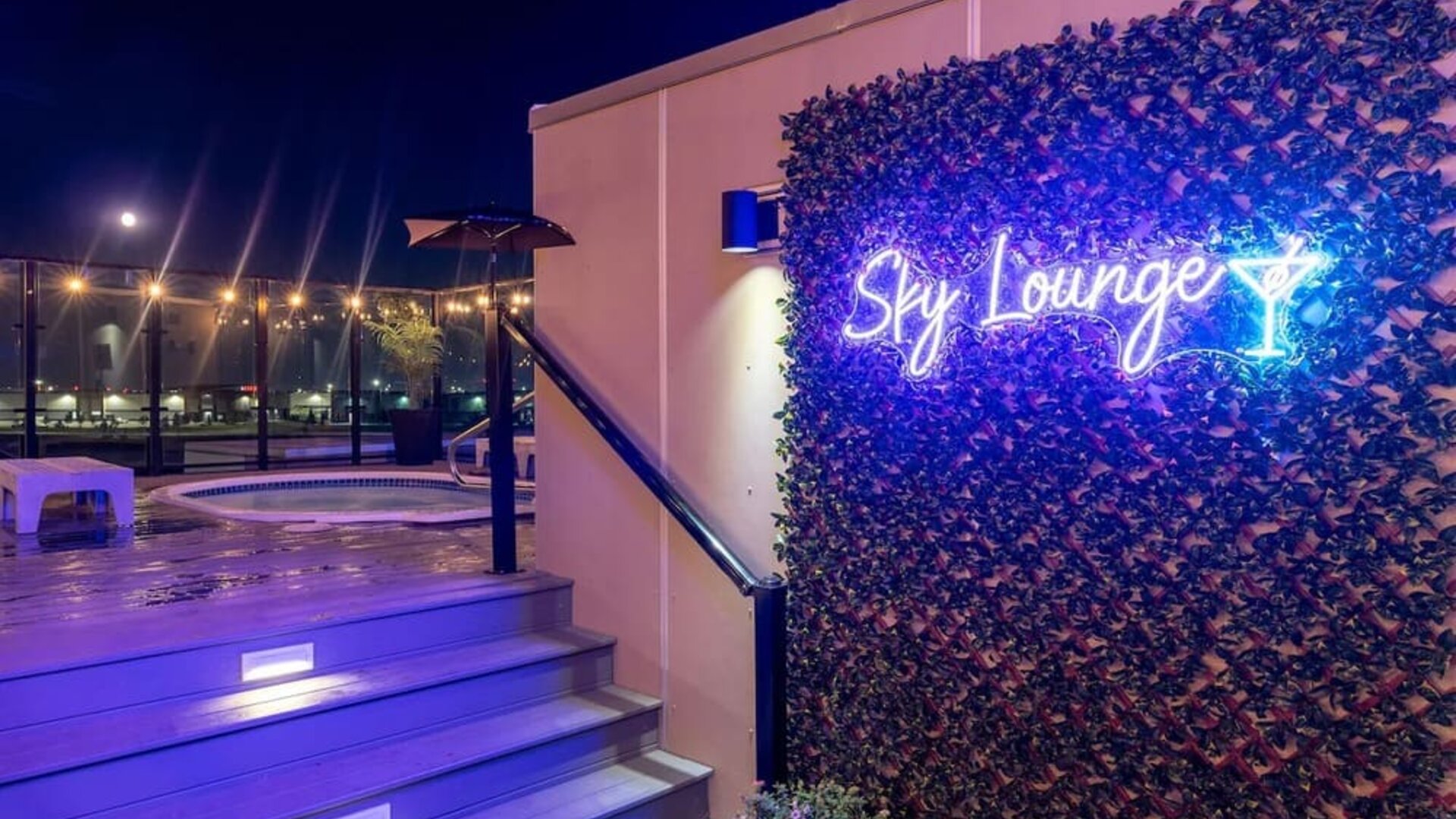 Rooftop Sky Lounge entrance with neon sign, illuminated steps, and hot tub area visible at night. Hotel Clique Calgary Airport.
