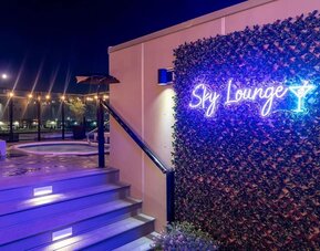 Rooftop Sky Lounge entrance with neon sign, illuminated steps, and hot tub area visible at night. Hotel Clique Calgary Airport.