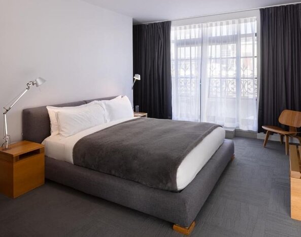 King guest room with floor-to-ceiling windows, modern lighting, lounge chair, and minimalist furnishings. Hotel Gault.