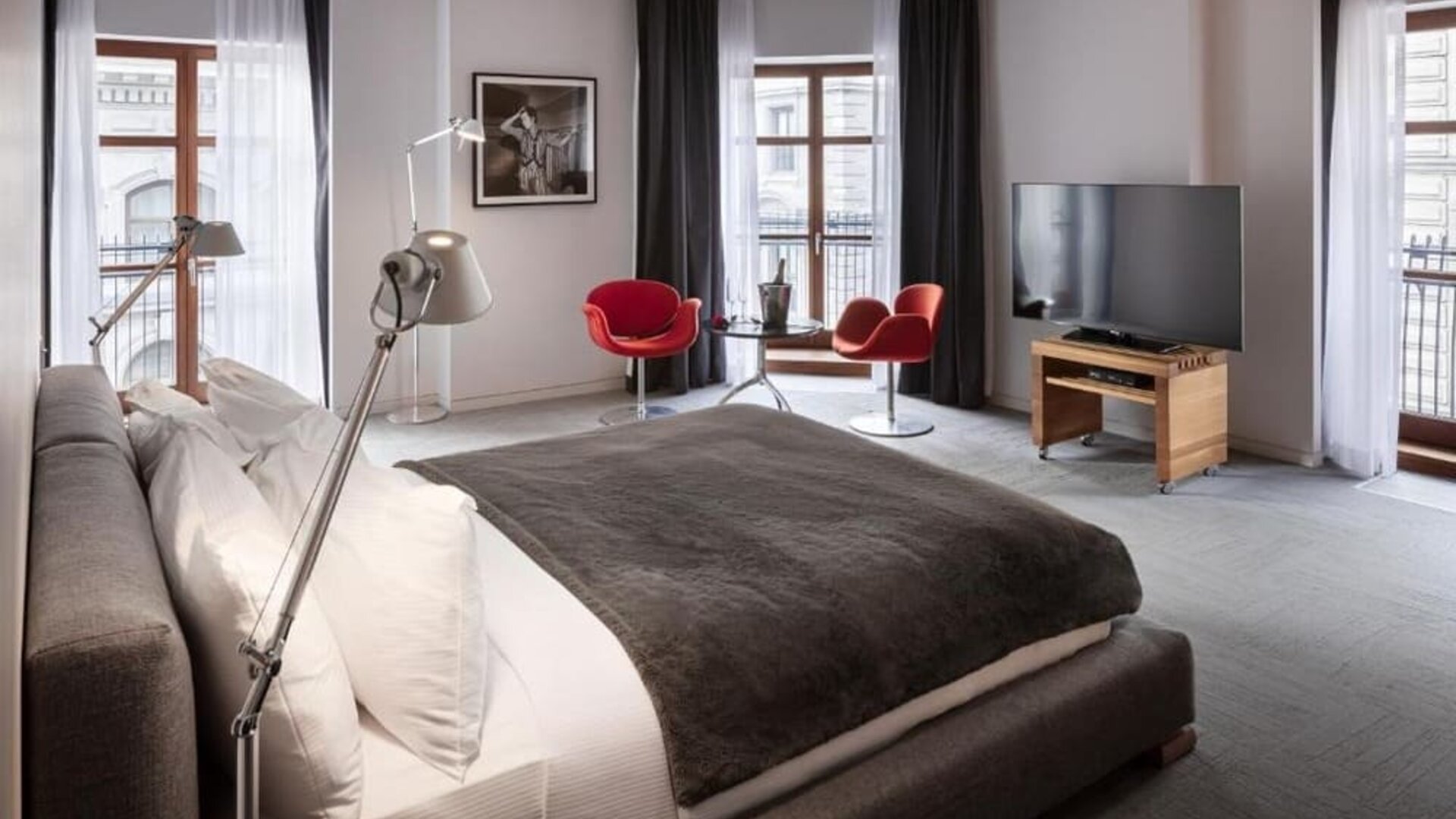 Spacious king guest room with large windows, red accent chairs, seating area, and flat-screen television. Hotel Gault.