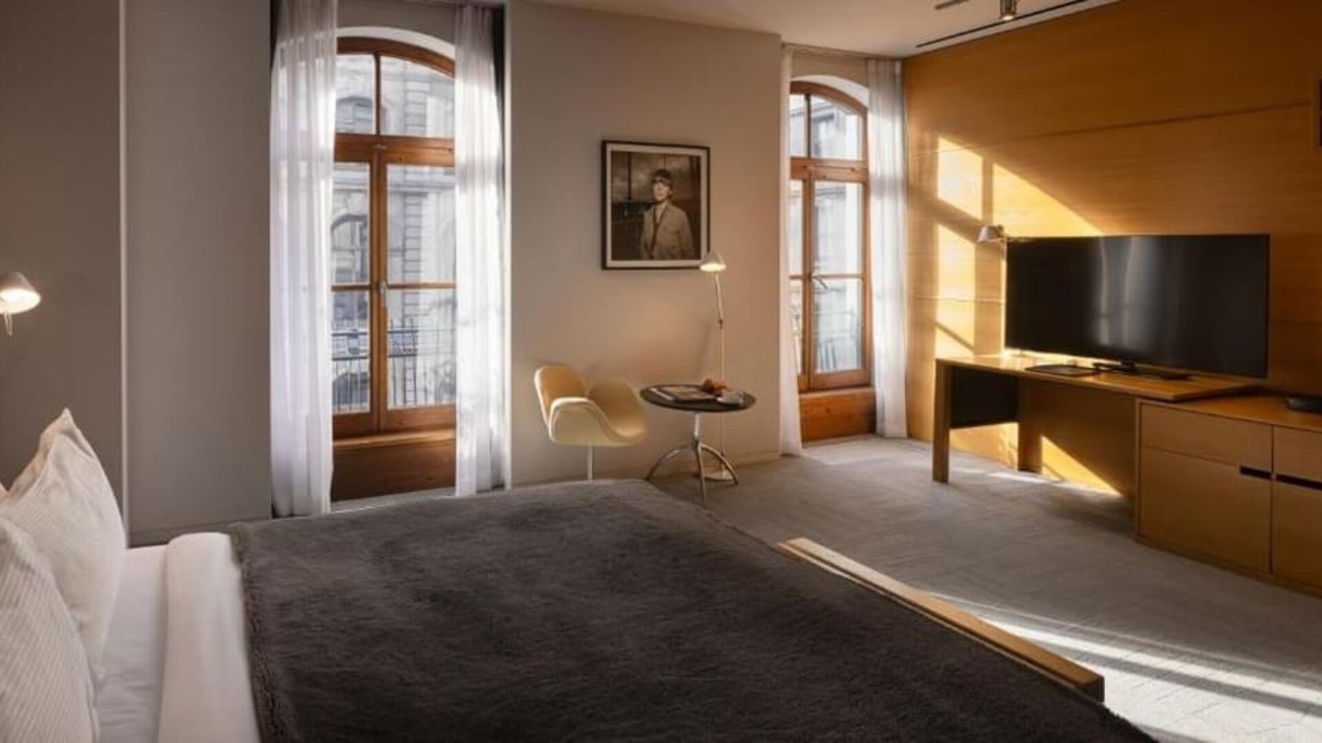 Spacious guest room with king bed, tall arched windows, seating area, and large flat-screen television. Hotel Gault.
