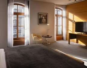 Spacious guest room with king bed, tall arched windows, seating area, and large flat-screen television. Hotel Gault.