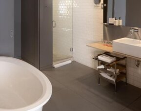 Modern bathroom with freestanding soaking tub, glass walk-in shower, floating vanity, and white subway tile walls. Hotel Gault.