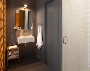 Modern bathroom with glass walk-in shower, floating vanity, open shelving, and white subway tile walls. Hotel Gault.