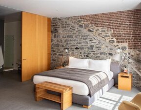 Guest room featuring an exposed stone and brick accent wall, king bed, and contemporary wooden furnishings. Hotel Gault.