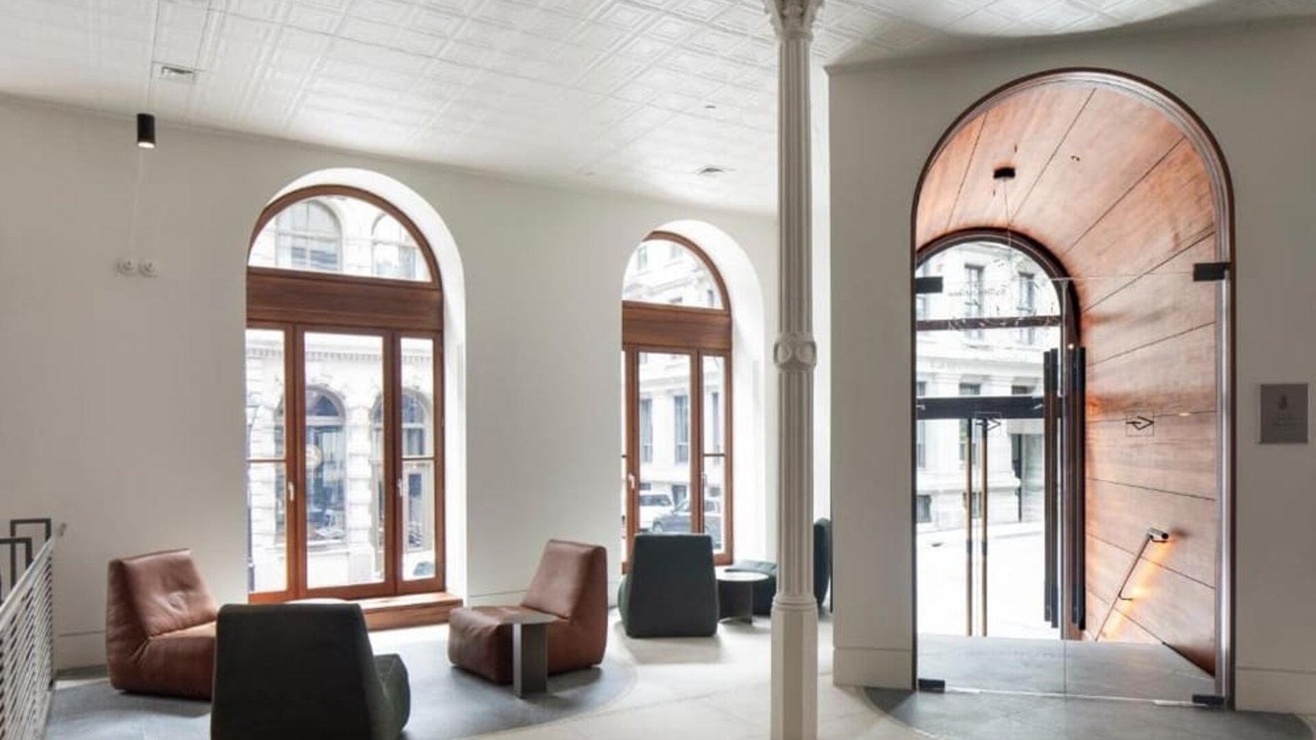 Bright hotel lobby with arched windows, modern lounge seating, and a large wooden entrance door. Hotel Gault.