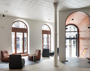 Bright hotel lobby with arched windows, modern lounge seating, and a large wooden entrance door. Hotel Gault.