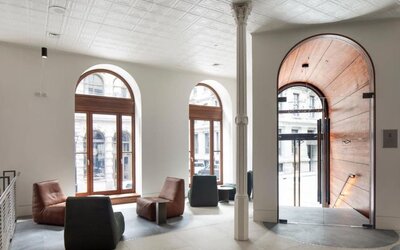 Bright hotel lobby with arched windows, modern lounge seating, and a large wooden entrance door. Hotel Gault.