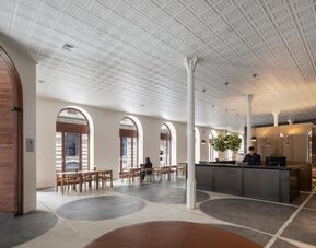 Spacious hotel lobby with reception desk, arched windows, dining tables, and contemporary seating areas. Hotel Gault.