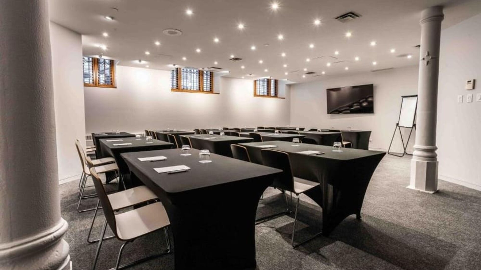 Meeting room with classroom-style table layout, presentation screen, flip chart, and overhead lighting. Hotel Gault.