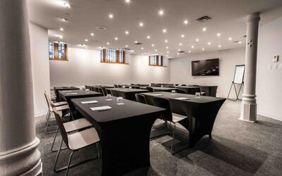 Meeting room with classroom-style table layout, presentation screen, flip chart, and overhead lighting. Hotel Gault.