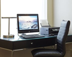 Business center workstation with desktop computer, printer, glass desk, and black leather office chair at Comfort Inn Boucherville.