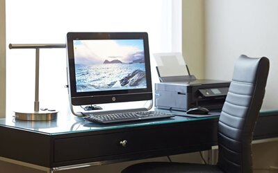 Business center workstation with desktop computer, printer, glass desk, and black leather office chair at Comfort Inn Boucherville.