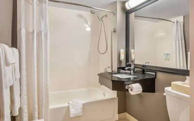 Accessible bathroom with bathtub and shower combination, grab bars, floating vanity, and large framed mirror at Comfort Inn Boucherville.