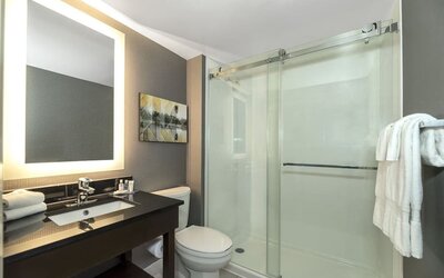 Modern bathroom with illuminated mirror, walk-in glass shower, black vanity, and fresh towels at Comfort Inn Boucherville.