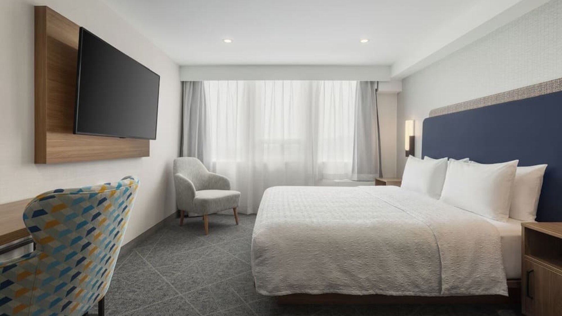 King guest room with large window, upholstered chair, wall-mounted television, and work area at Hampton Inn By Hilton Montreal East Anjou.