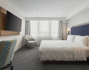 King guest room with large window, upholstered chair, wall-mounted television, and work area at Hampton Inn By Hilton Montreal East Anjou.
