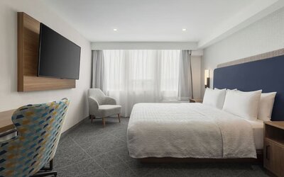 King guest room with large window, upholstered chair, wall-mounted television, and work area at Hampton Inn By Hilton Montreal East Anjou.
