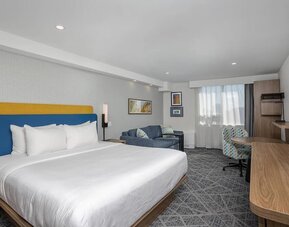Spacious king guest room with sofa, work desk, and large television at Hampton Inn By Hilton Montreal East Anjou.