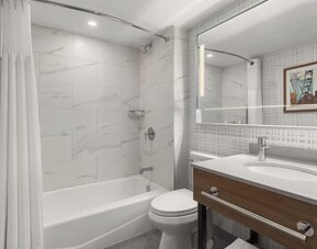Modern bathroom with bathtub and shower combination, illuminated mirror, and wood vanity at Hampton Inn By Hilton Montreal East Anjou.