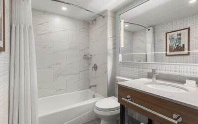 Modern bathroom with bathtub and shower combination, illuminated mirror, and wood vanity at Hampton Inn By Hilton Montreal East Anjou.