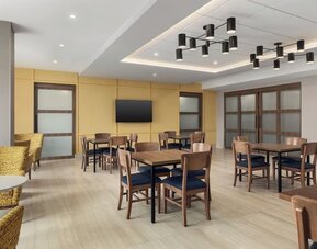 Bright breakfast dining area with wooden tables, cushioned chairs, and modern ceiling lighting at Hampton Inn By Hilton Montreal East Anjou.