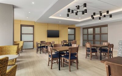 Bright breakfast dining area with wooden tables, cushioned chairs, and modern ceiling lighting at Hampton Inn By Hilton Montreal East Anjou.