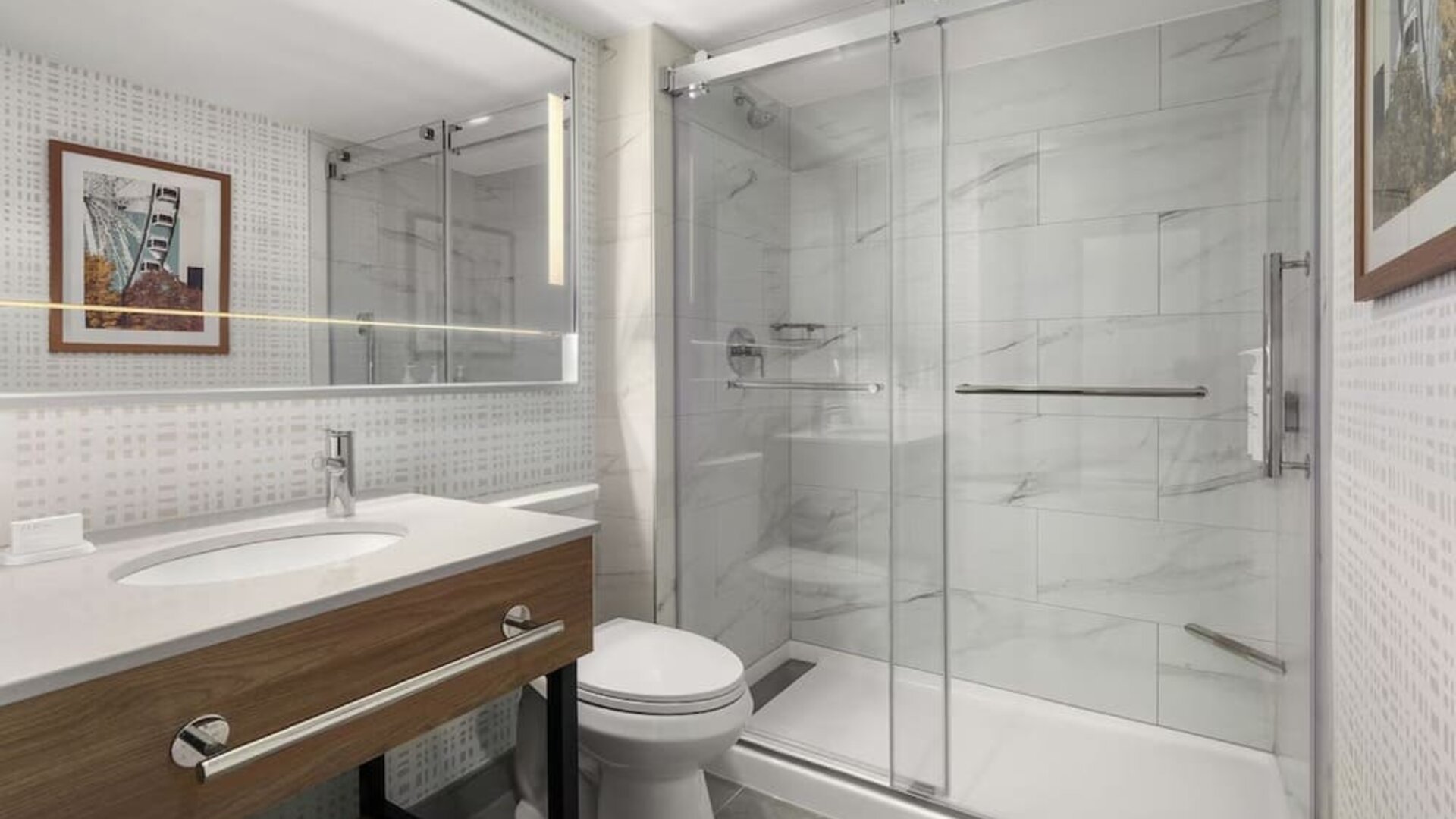 Accessible bathroom with roll-in glass shower, grab bars, illuminated mirror, and modern vanity at Hampton Inn By Hilton Montreal East Anjou.
