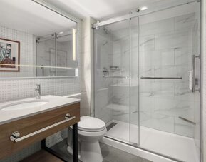 Accessible bathroom with roll-in glass shower, grab bars, illuminated mirror, and modern vanity at Hampton Inn By Hilton Montreal East Anjou.