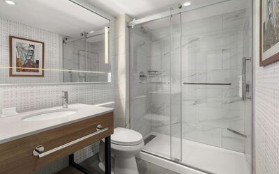 Accessible bathroom with roll-in glass shower, grab bars, illuminated mirror, and modern vanity at Hampton Inn By Hilton Montreal East Anjou.