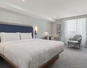 Spacious king guest room with seating area, work desk, large window, and contemporary furnishings at Hampton Inn By Hilton Montreal East Anjou.